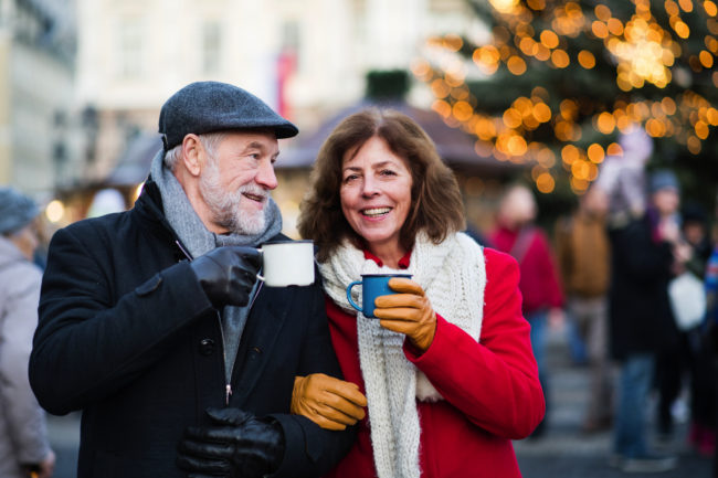Happy senior couple on an outdoor Christmas market, drinking tea or coffee. Winter time.